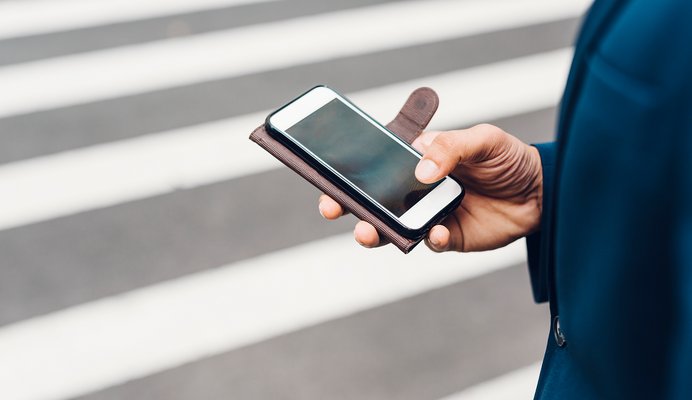 Hand hält Smartphone auf Zebrastreifen.