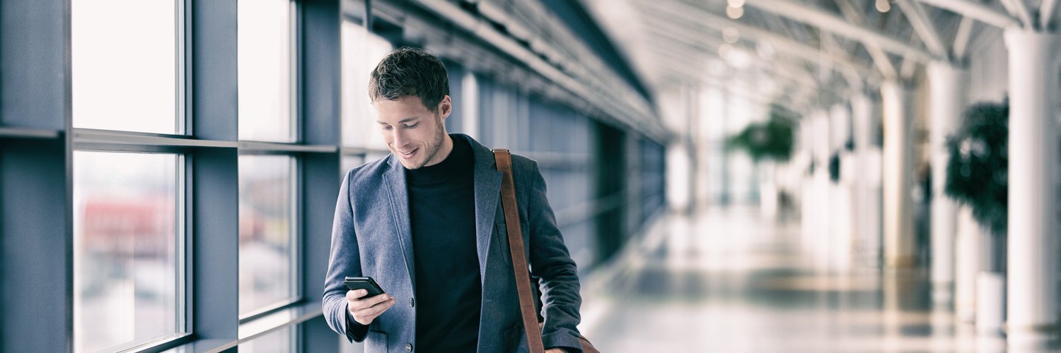 Junger Mann geht einen Flur entlang und schaut auf sein Smartphone.