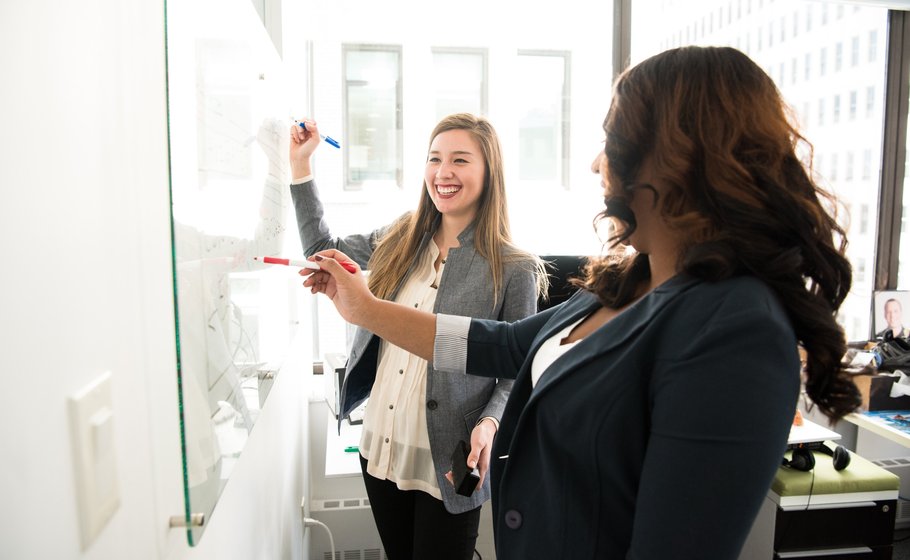 Zwei Frauen lächeln an Whiteboard.