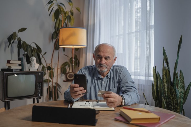 Älterer Herr mit Smartphone und Debitkarte.
